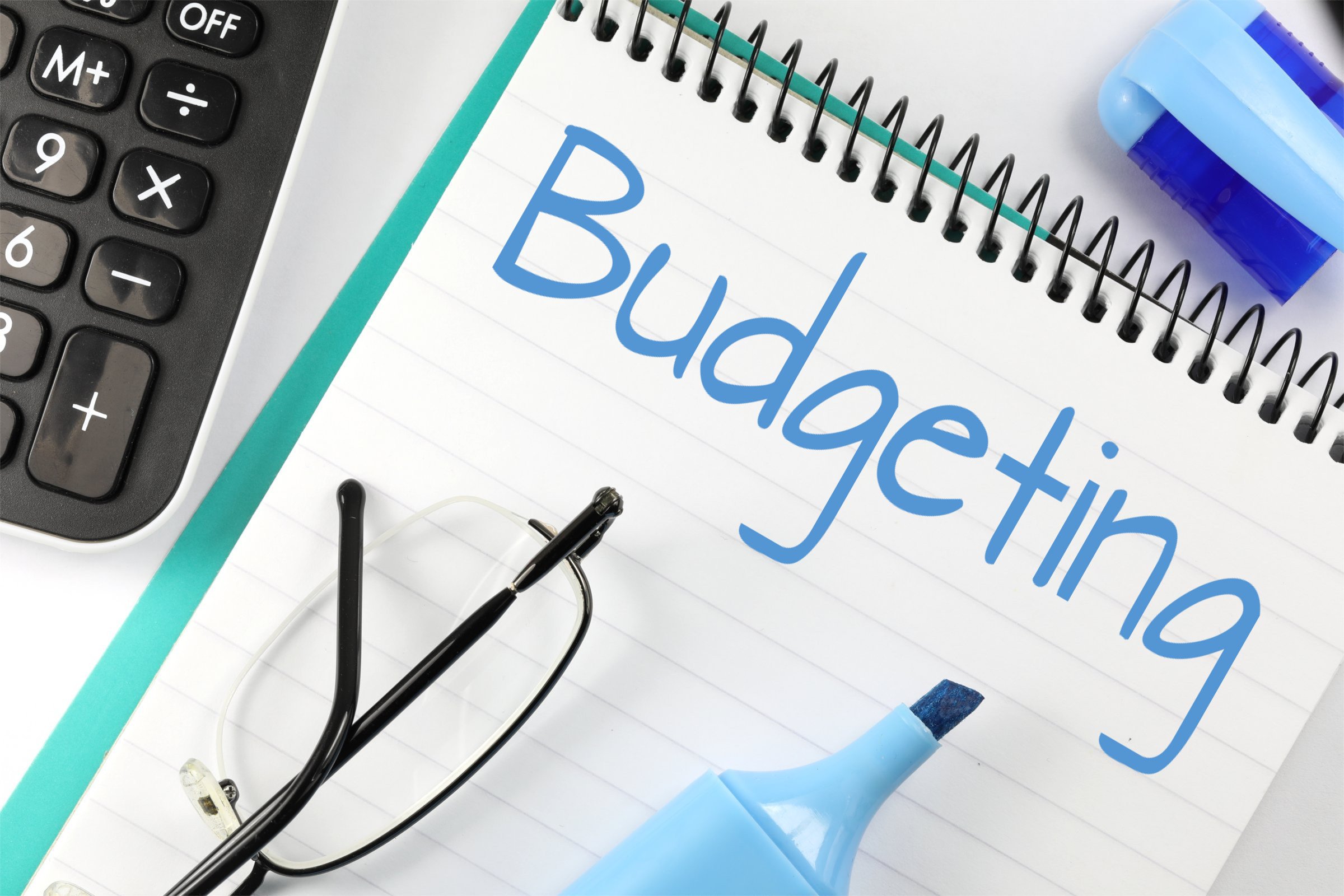 Caderno com a palavra 'budgeting', caneta e calculadora (planejamento de gastos)